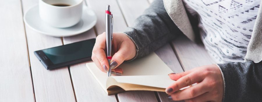 Best Journal Tips For Beginners Graphic Of Woman Writing In Her Journal On A White Wooden Table