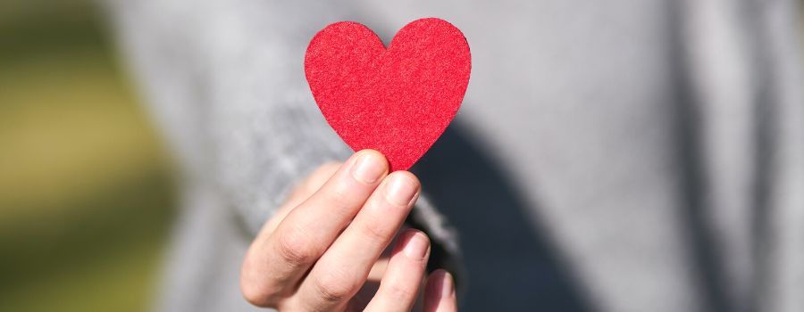 Self Love Affirmations Graphic Of Women In Grey Sweater Holding A Red Paper Heart